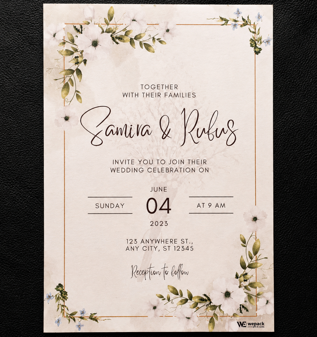 A rectangular wedding invitation card with a cream background, delicate floral watercolor illustrations in green and white, and thin gold border lines. The card features elegant black and cursive text reading 'Together with their families, Samira & Rufus invite you to join their wedding celebration on Sunday 04 June 2023 at 9 am' and is photographed flat against a dark textured background.