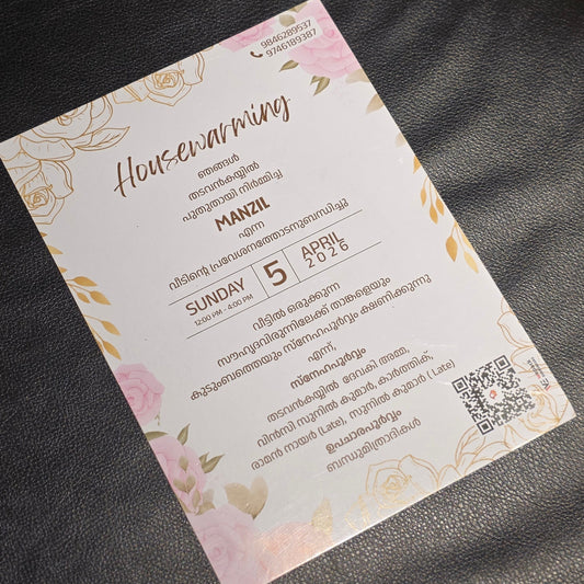 A rectangular printed card with floral pink and gold border design, photographed on a dark textured surface. The card contains event text in English and Thai, including the heading 'Housewarming' and details for a Sunday 5 PM event.