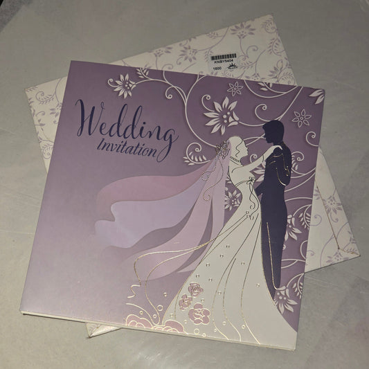 A square wedding invitation card with a lavender and white floral design featuring a bride and groom silhouette, placed on top of a matching patterned envelope on a light surface.