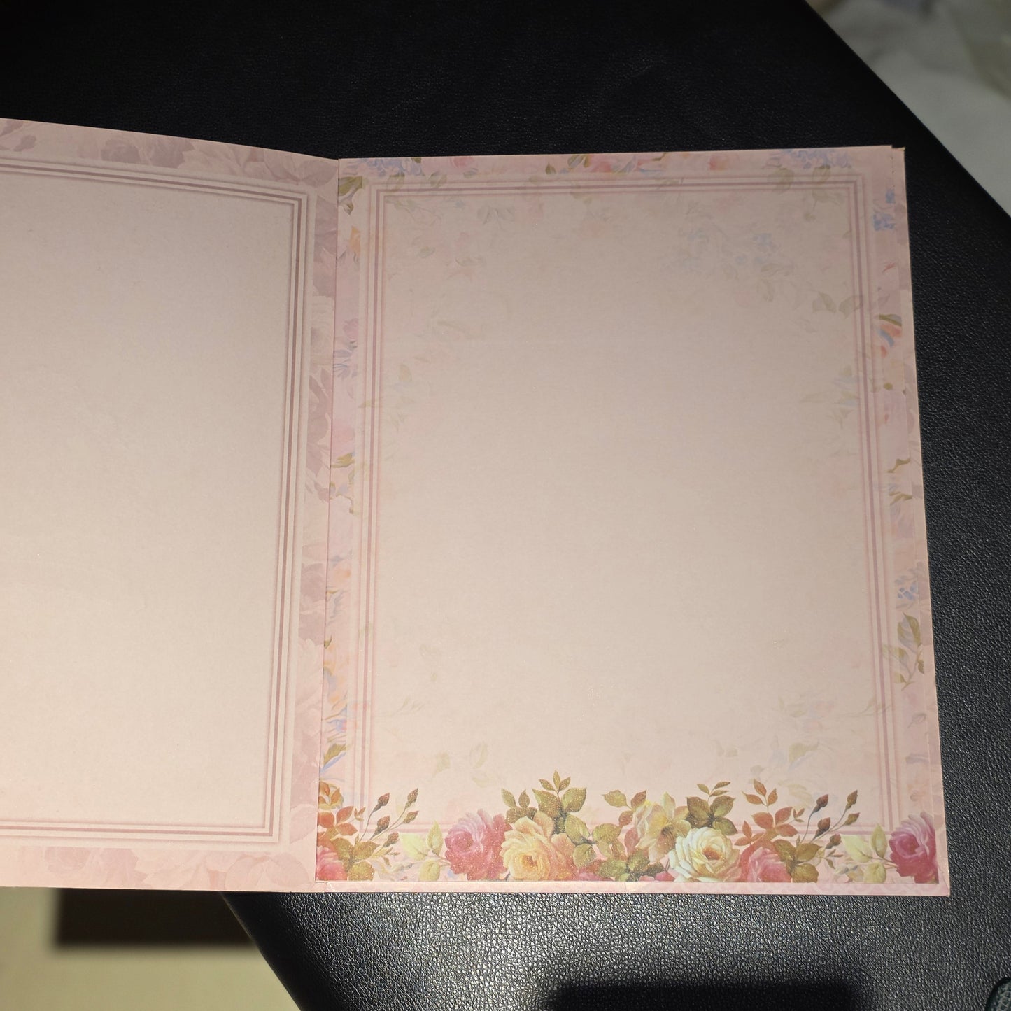 An open pink notepad or stationery card with a delicate floral border and a small bouquet of flowers along the bottom edge, photographed on a dark surface.