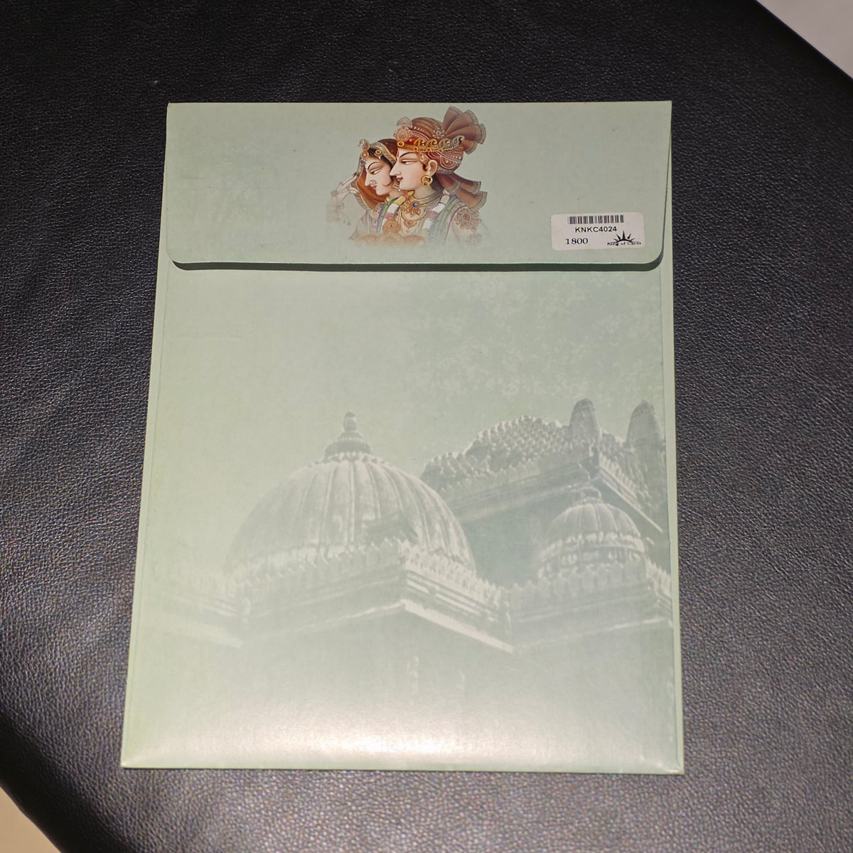 A mint green envelope or card with a faded architectural dome illustration and a small character print near the top, placed on a dark textured surface.