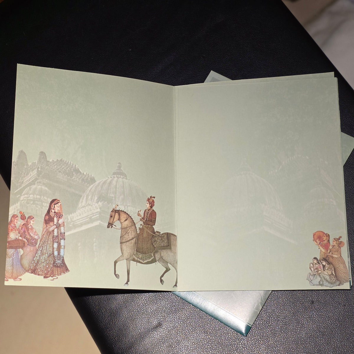 An open book or booklet lying on a dark textured surface, showing illustrated pages with a pale greenish tint and faint vintage-style drawings of domed architecture and small figures.
