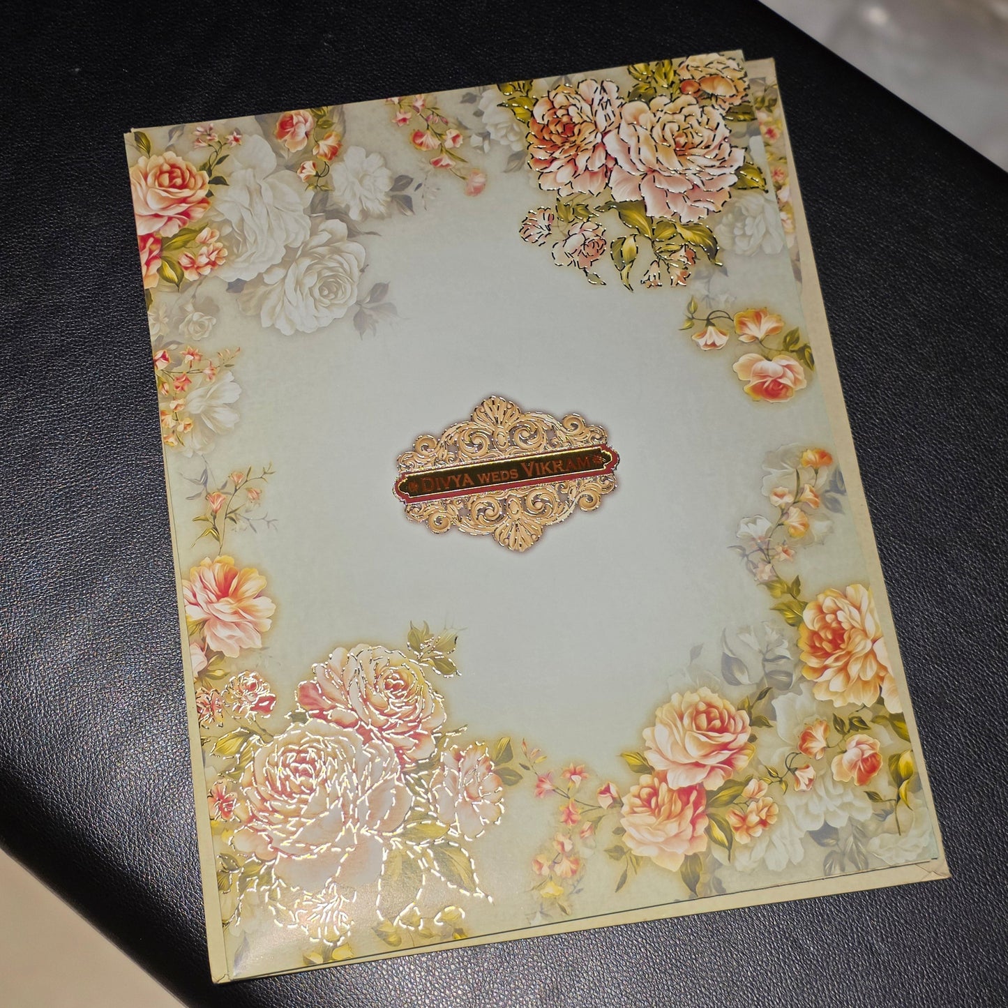 A rectangular decorative card or envelope with a vintage floral border and a central ornate label, photographed on a dark textured surface.