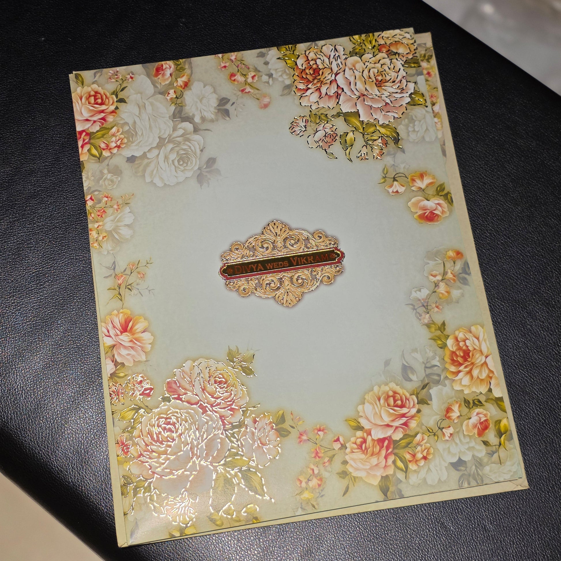 A rectangular decorative card or envelope with a vintage floral border and a central ornate label, photographed on a dark textured surface.