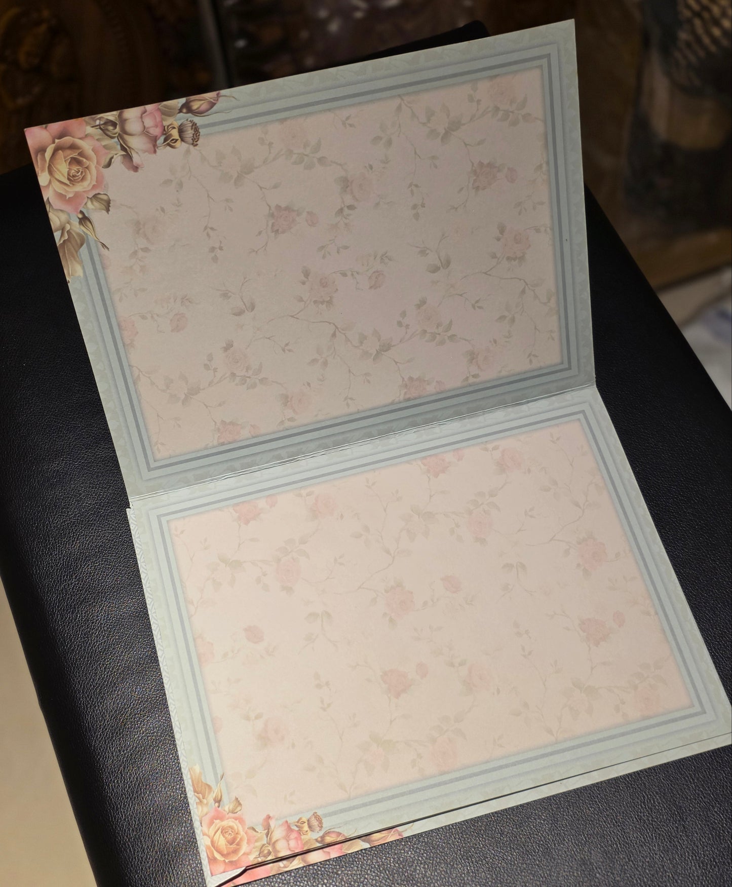 An open notebook or journal with pale pink floral patterned pages and a light blue border, photographed on a dark textured surface.