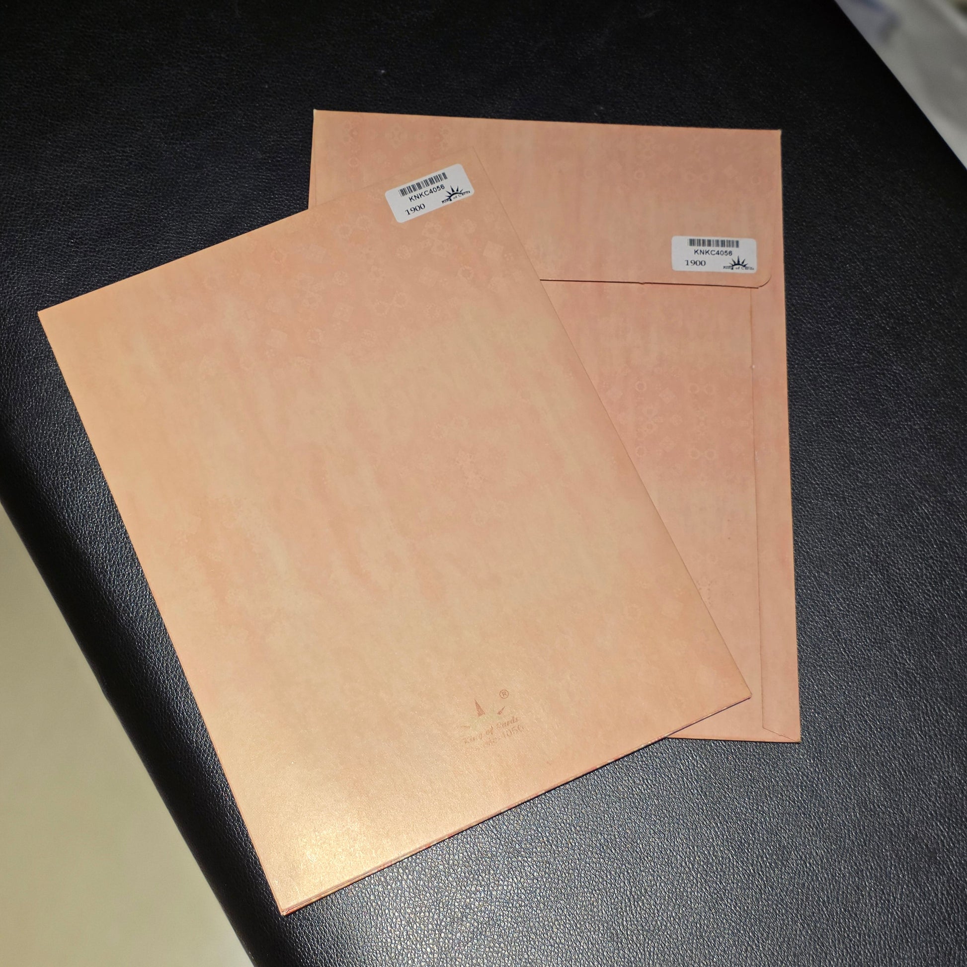 Two square sheets of copper-colored metal or wood with small white labels, resting on a black textured surface.