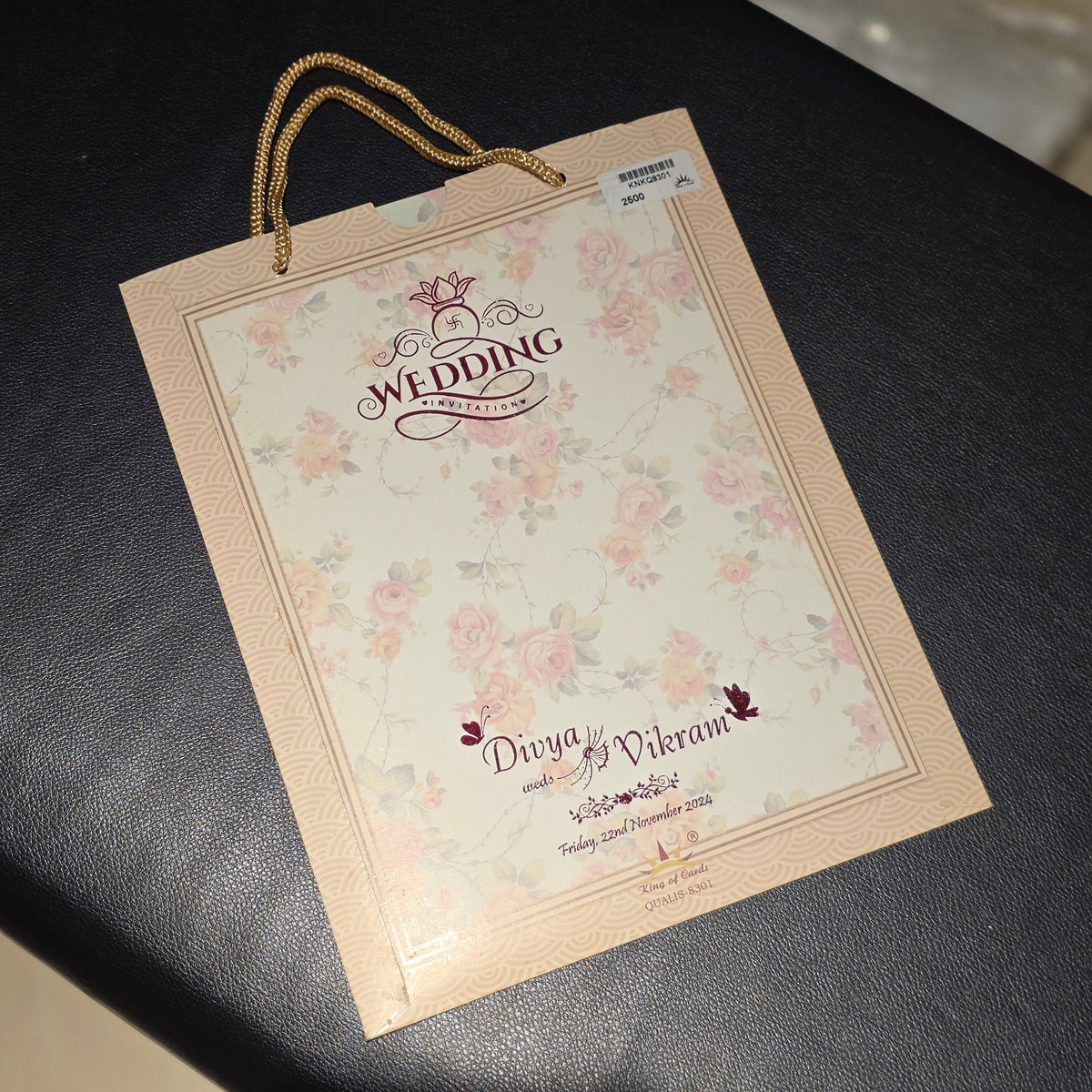 A personalized wedding gift bag with floral print and gold rope handles, placed on a dark textured surface.