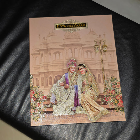 A rectangular printed card or postcard featuring an illustrated traditional wedding scene with two elegantly dressed couples seated in front of a palace, placed on a black leather surface.