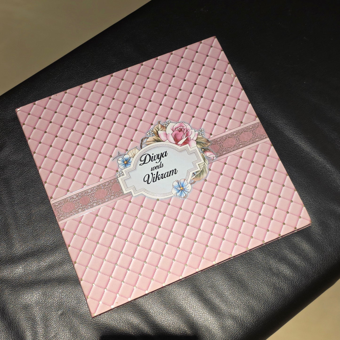 A square pink quilted card or decorative cover with a central floral label reading 'Dieye and Vibram,' placed on a black leather-like surface.
