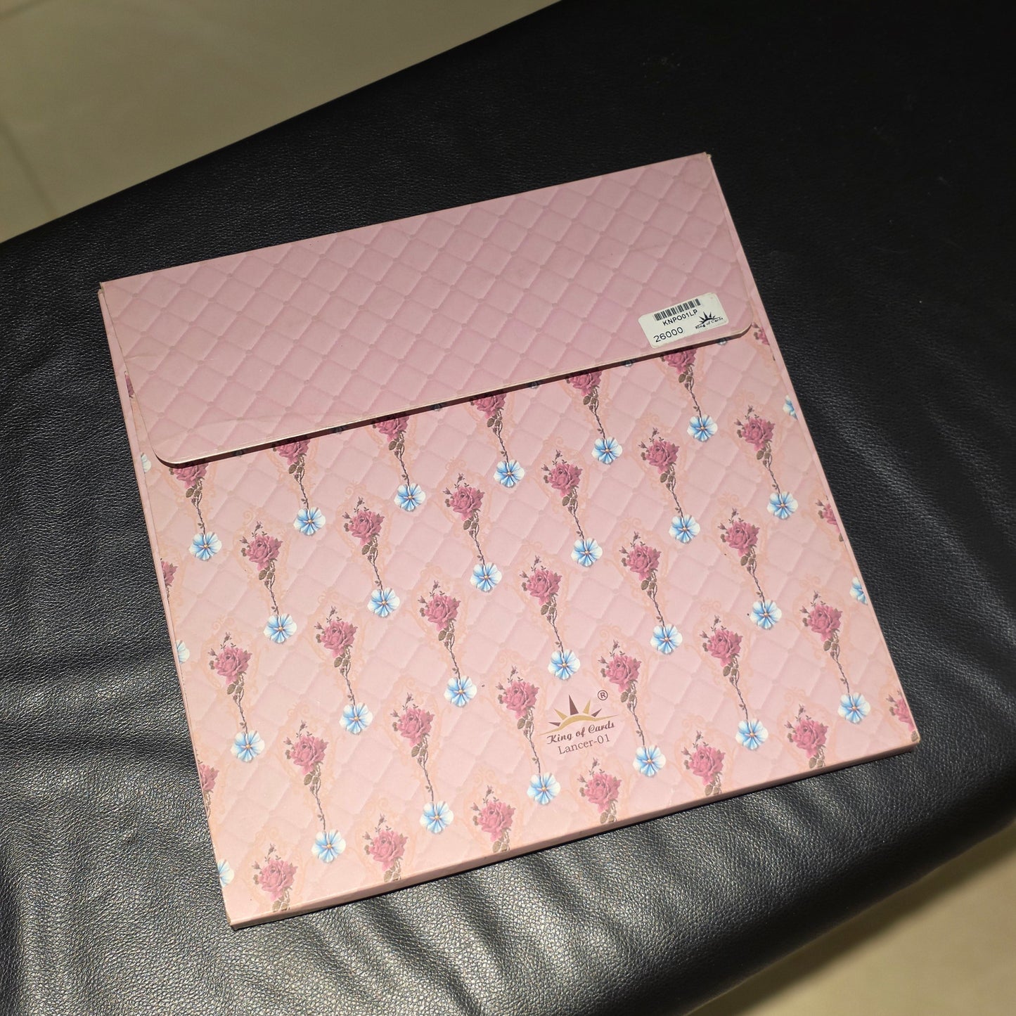 A pink quilted envelope-style pouch with a floral pattern, placed on a black leather surface.