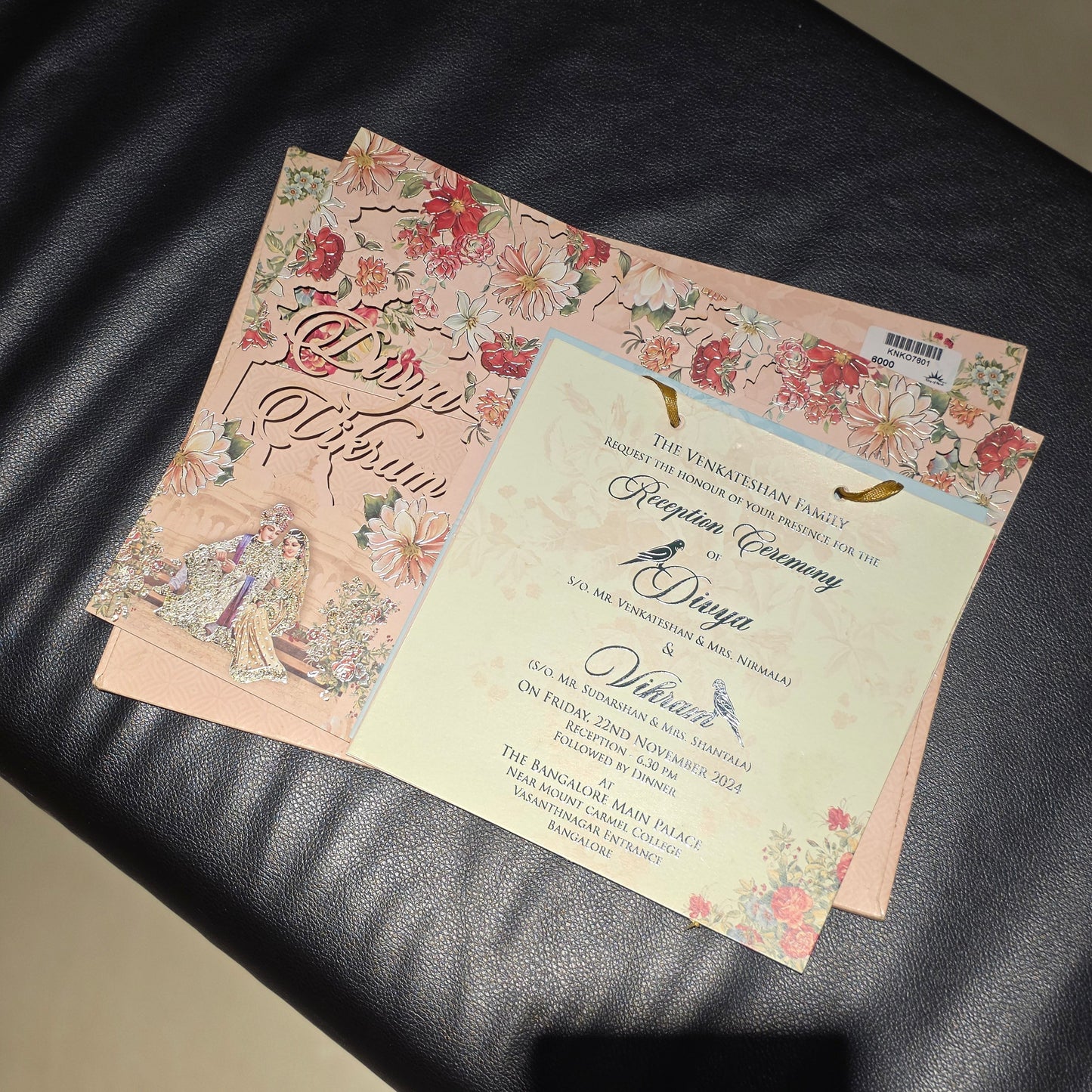 A stack of printed invitation cards or stationery pieces with floral borders and elegant script text, placed on a black leather surface.
