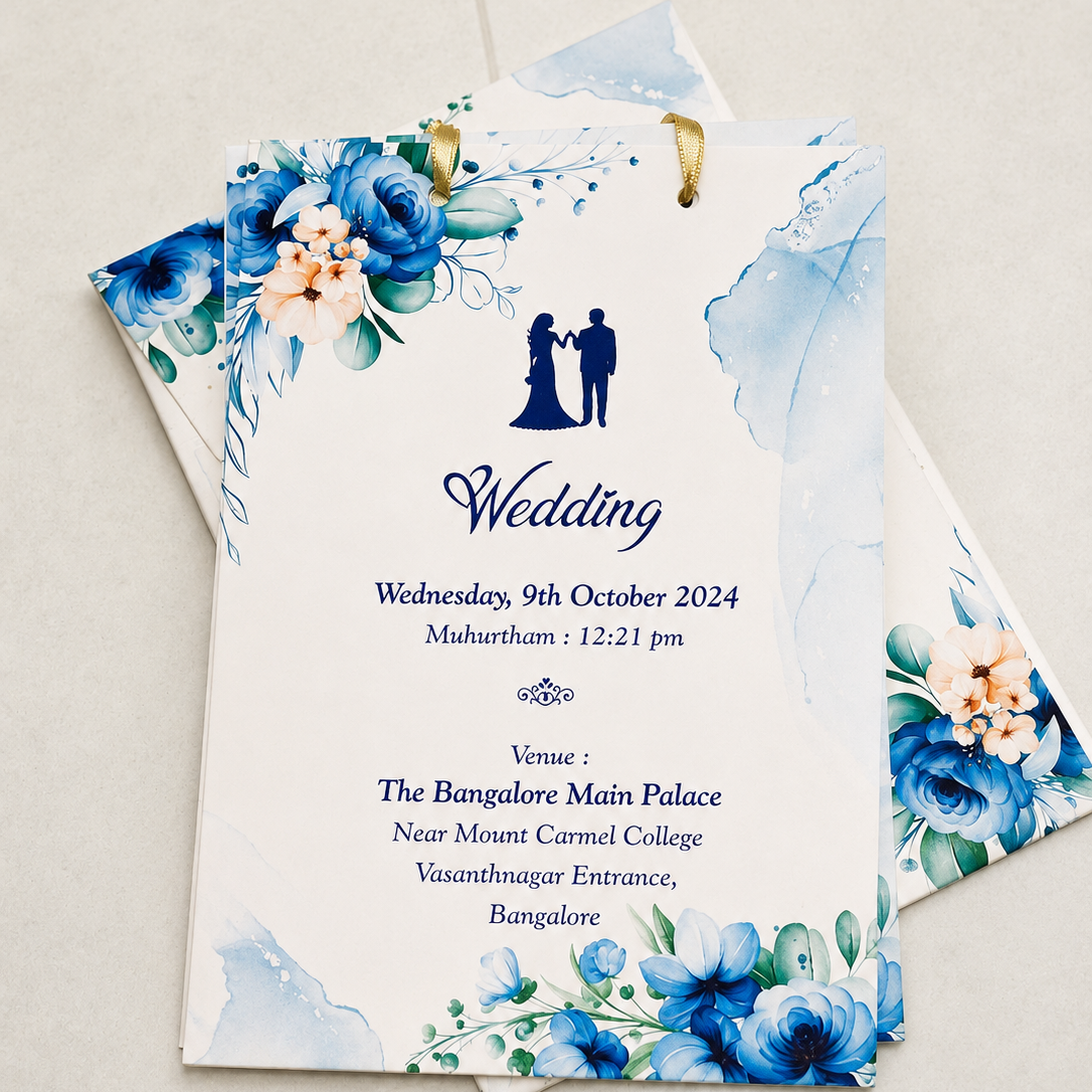 A wedding invitation card with elegant blue watercolor floral designs and a navy blue silhouette of a couple, displayed on a light beige textured background.
