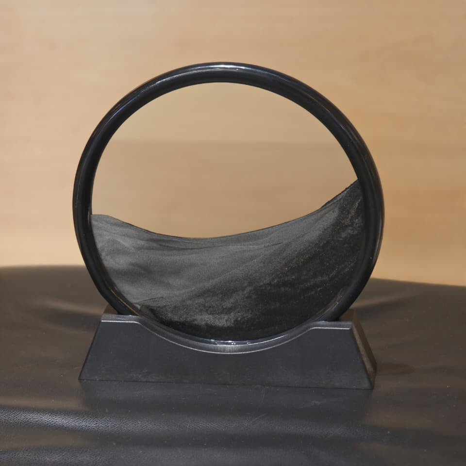 A black circular ring-shaped object displayed on a black stand against a light wood background.