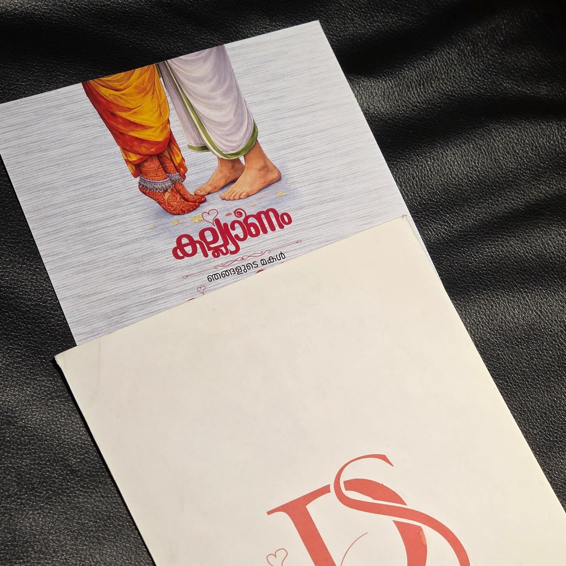 A close-up of printed cards or a booklet laid on a black leather surface. One card shows a small illustration with the word 'encanto' in red script, and the other shows a large red stylized 'DS' logo on a white background with a QR code.