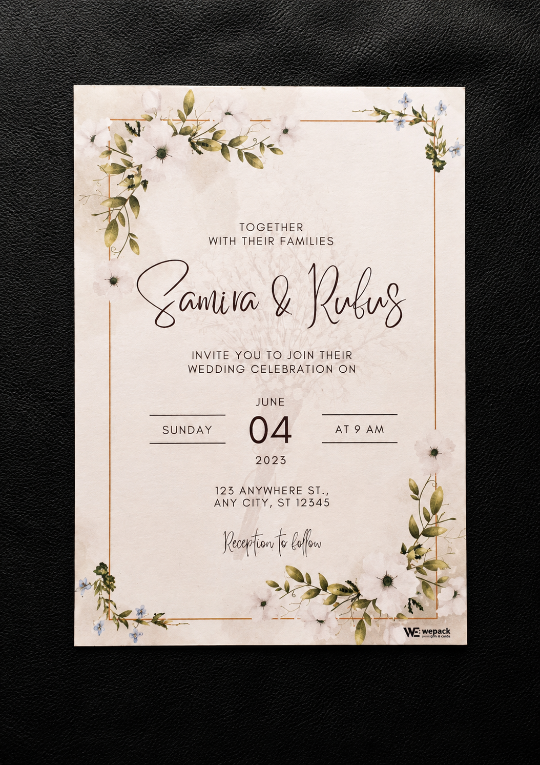A rectangular wedding invitation card with a cream background, delicate floral watercolor illustrations in green and white, and thin gold border lines. The card features elegant black and cursive text reading 'Together with their families, Samira & Rufus invite you to join their wedding celebration on Sunday 04 June 2023 at 9 am' and is photographed flat against a dark textured background.