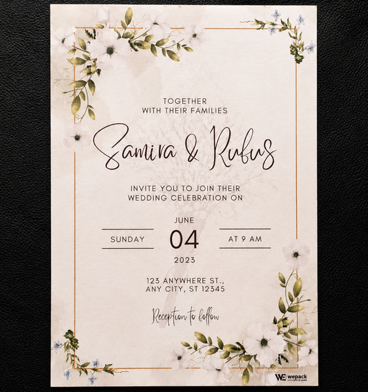 A rectangular wedding invitation card with a cream background, delicate floral watercolor illustrations in green and white, and thin gold border lines. The card features elegant black and cursive text reading 'Together with their families, Samira & Rufus invite you to join their wedding celebration on Sunday 04 June 2023 at 9 am' and is photographed flat against a dark textured background.